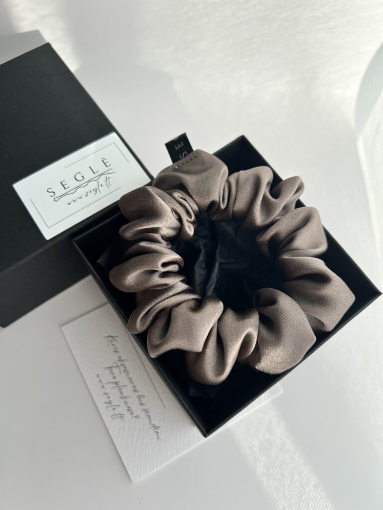 Natūralaus šilko rusvai pilkos spalvos plaukų gumytė juodoje dėžutėje baltame fone