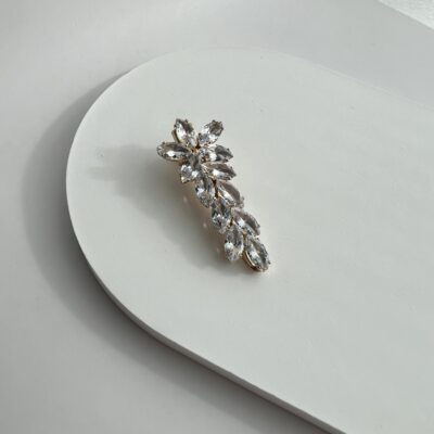 Metalinis plaukų segtukas dekoruotas blizgančiais cirkoniais. Metalo spalva - auksinė. Cirkoniai išdėstyti gėlės forma