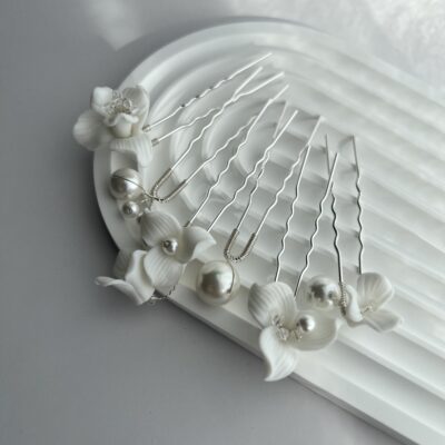 Metaliniai smeigtukai plaukams dekoruoti baltomis gėlėmis ir dirbtiniais perlais. Metalas sidabro spalvos. Smeigtukai baltame fone ant balto keramikinio padėkliuko