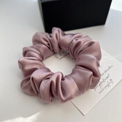 Natūralaus šilko šaltos rausvos spalvos šilkinė plaukų gumytė baltame fone šalia juodos dėžutės